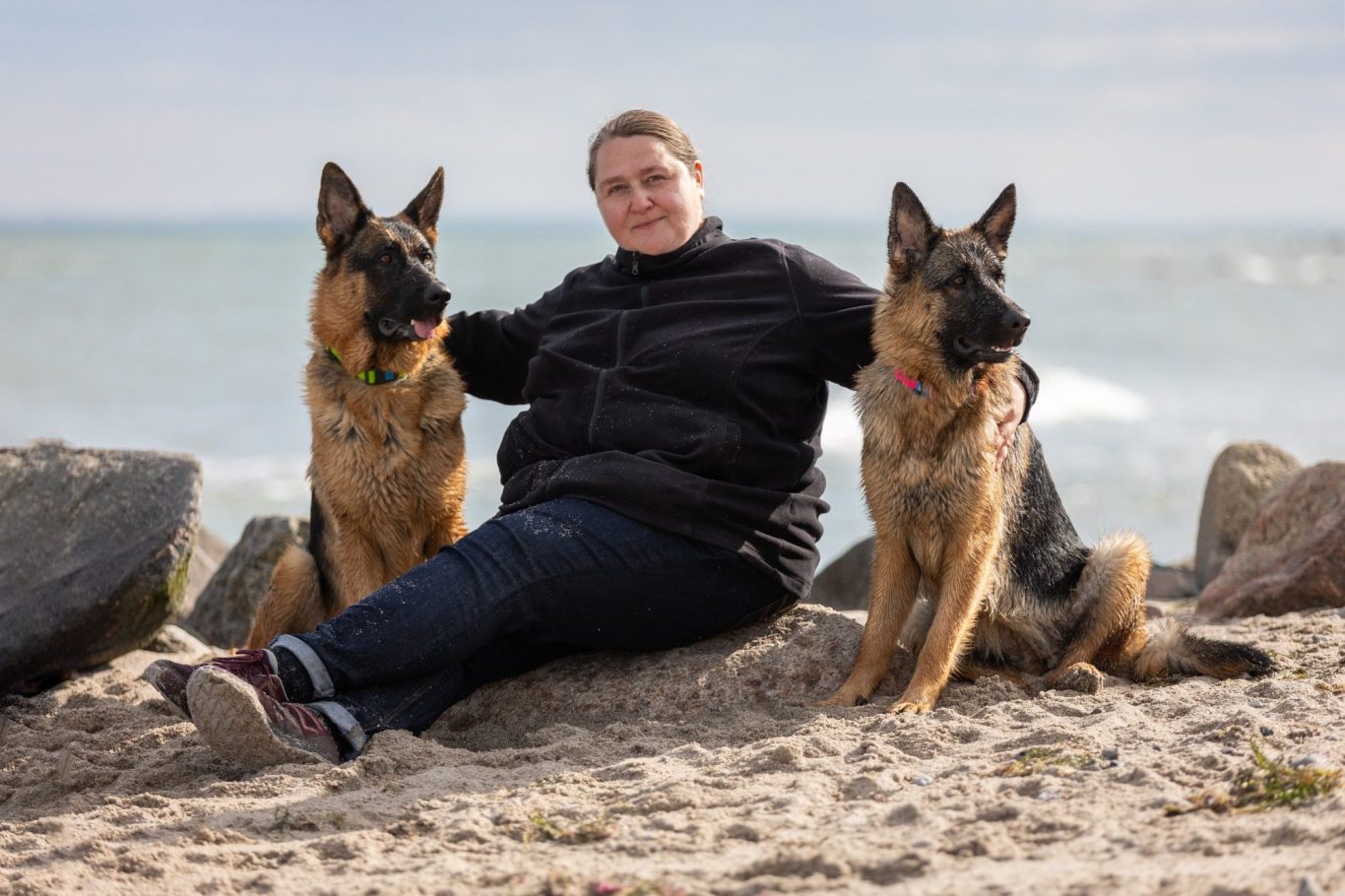 Fotografin Violetta Hanau sitzt am Strand zwischen zwei Deutschen Schäferhunden.