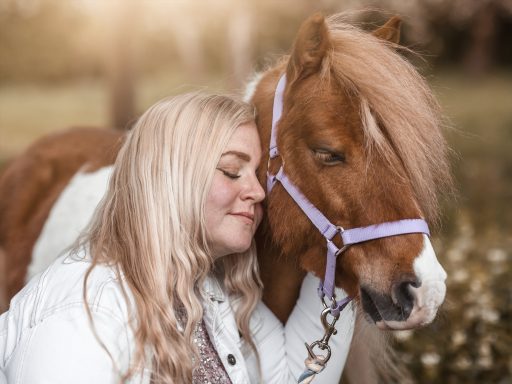 Ein Mädchen umarmt einen kleinen, braunen Pony mit einer lila Trense.
